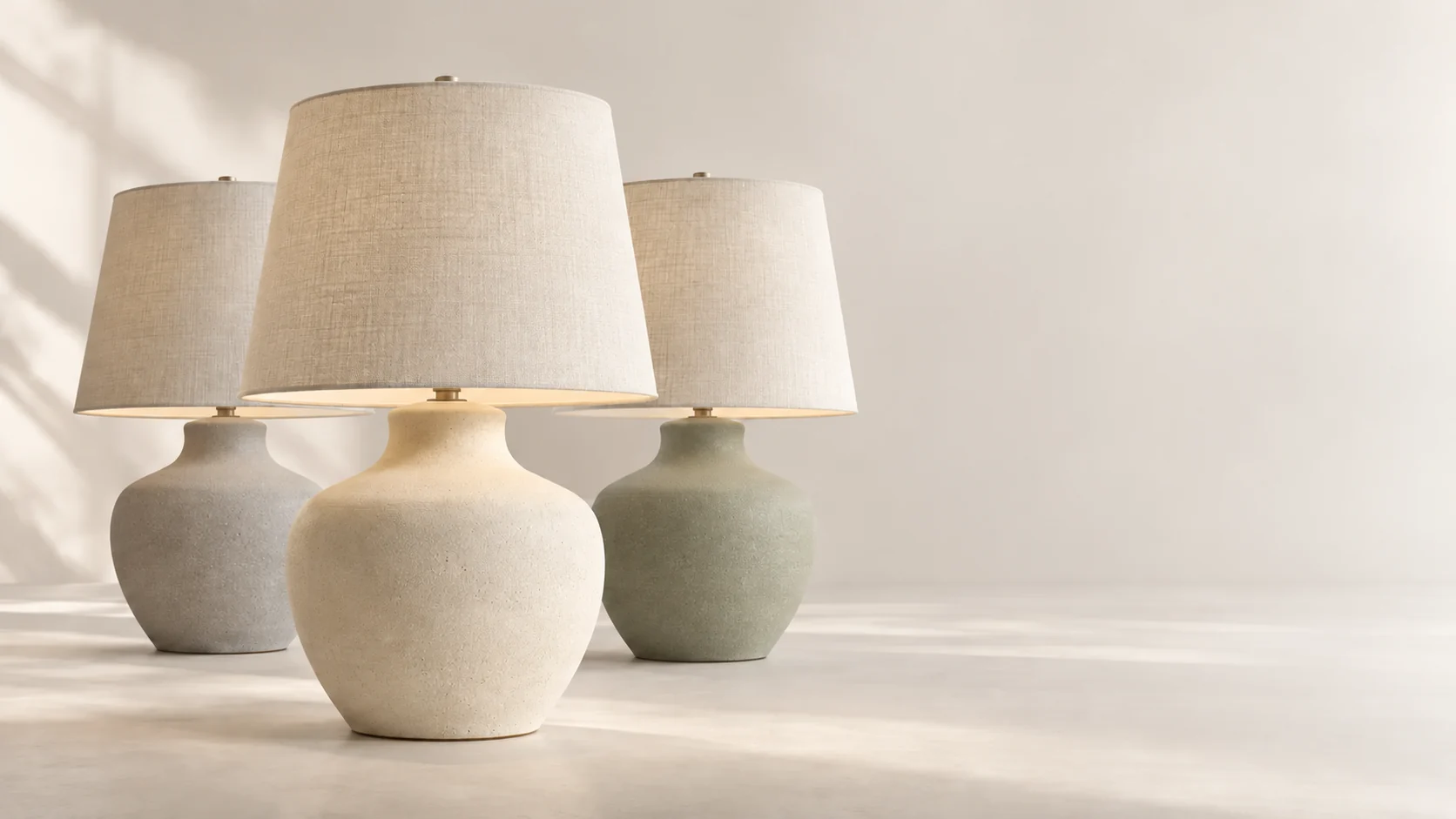 Três luminárias de mesa em tons neutros, com diferentes acabamentos, organizadas em um estúdio claro.